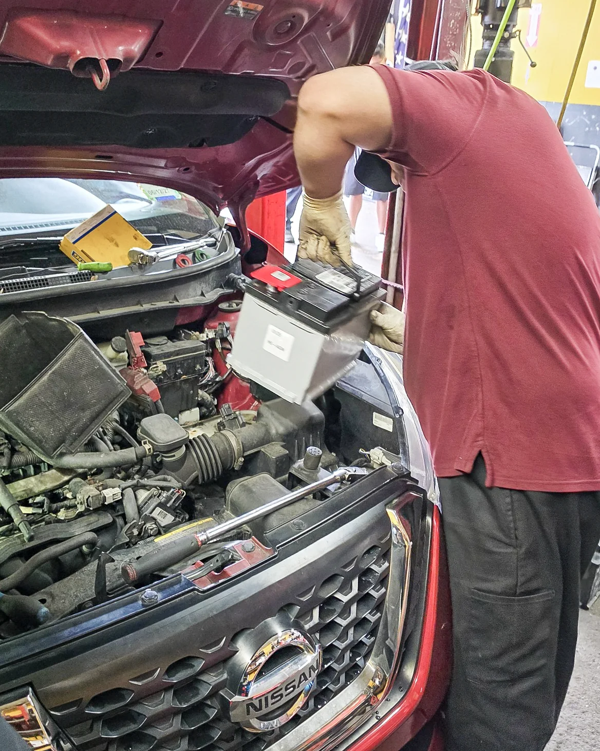Mechanic installing a battery in a red vehicle